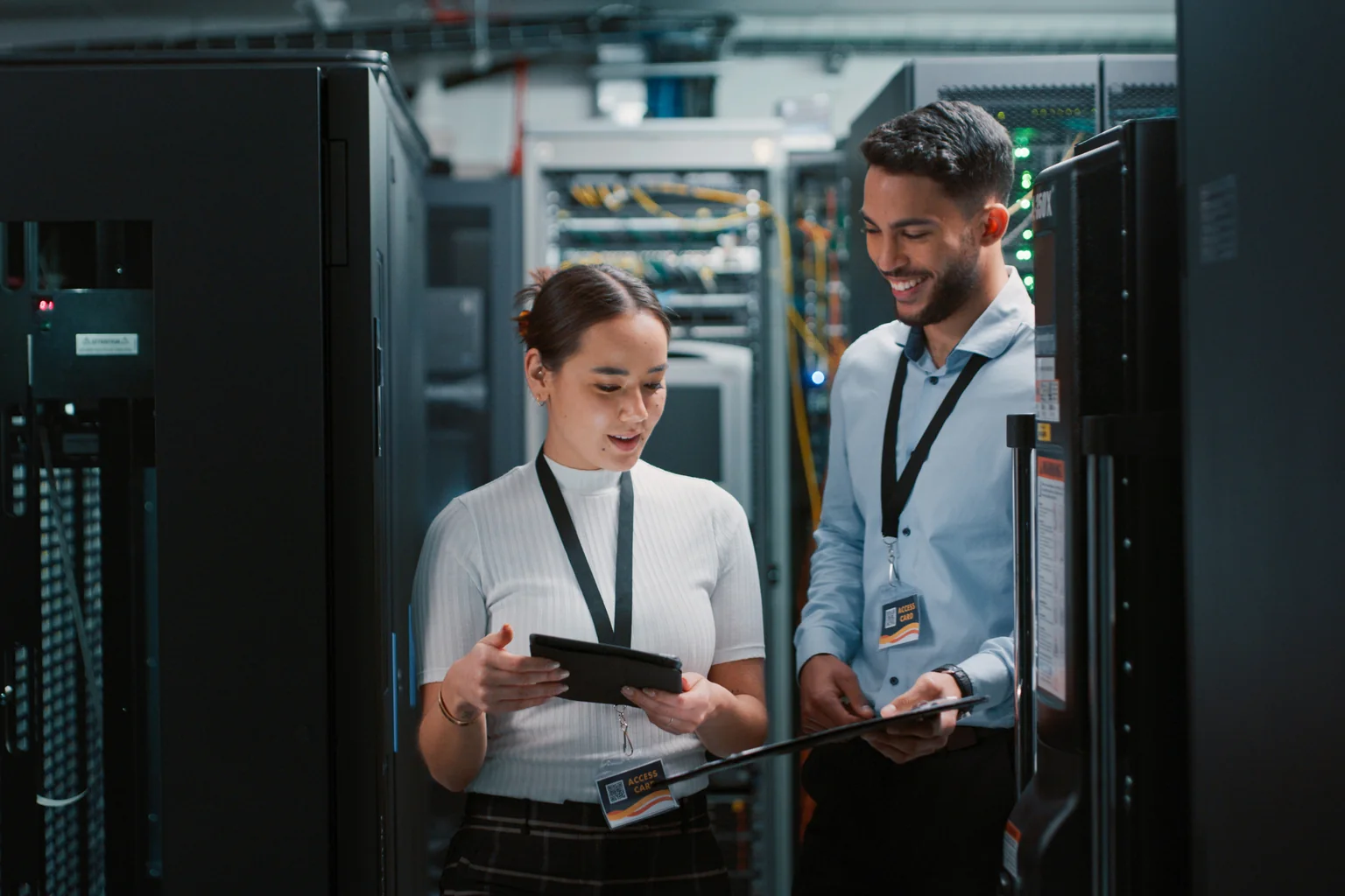 Two engineers reviewing a tablet between server racks in a data hall.