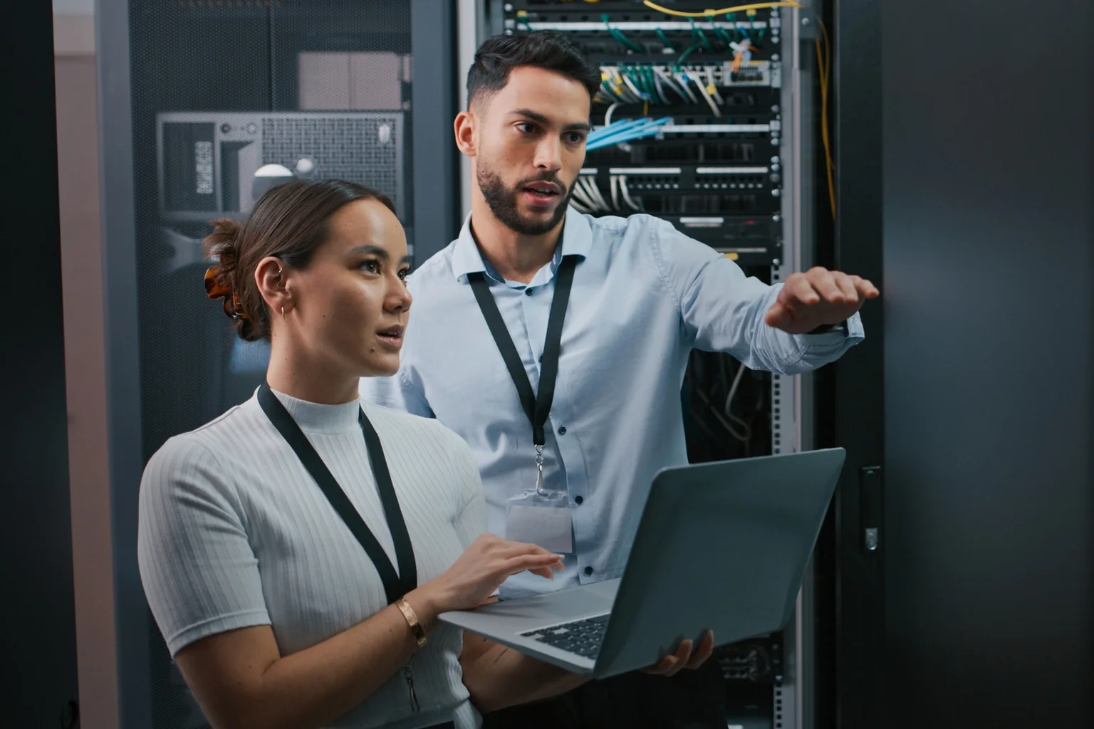 Two engineers reviewing a laptop beside an open server cabinet.