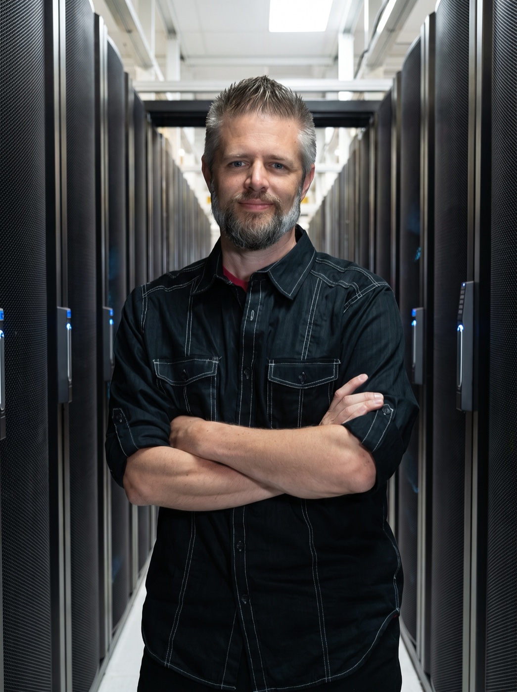 An Opus Interactive team member standing with arms crossed in a data-center aisle between rows of server cabinets