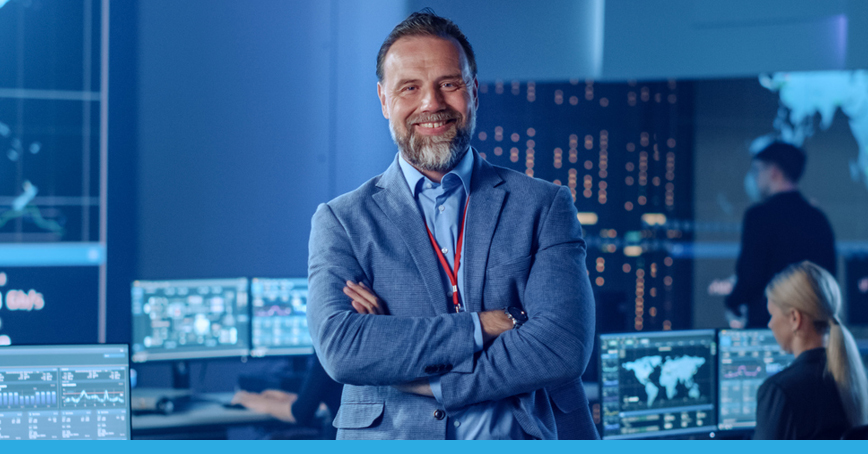 An image that depicts a CIO smiling at the viewer in a room of network monitoring operations.