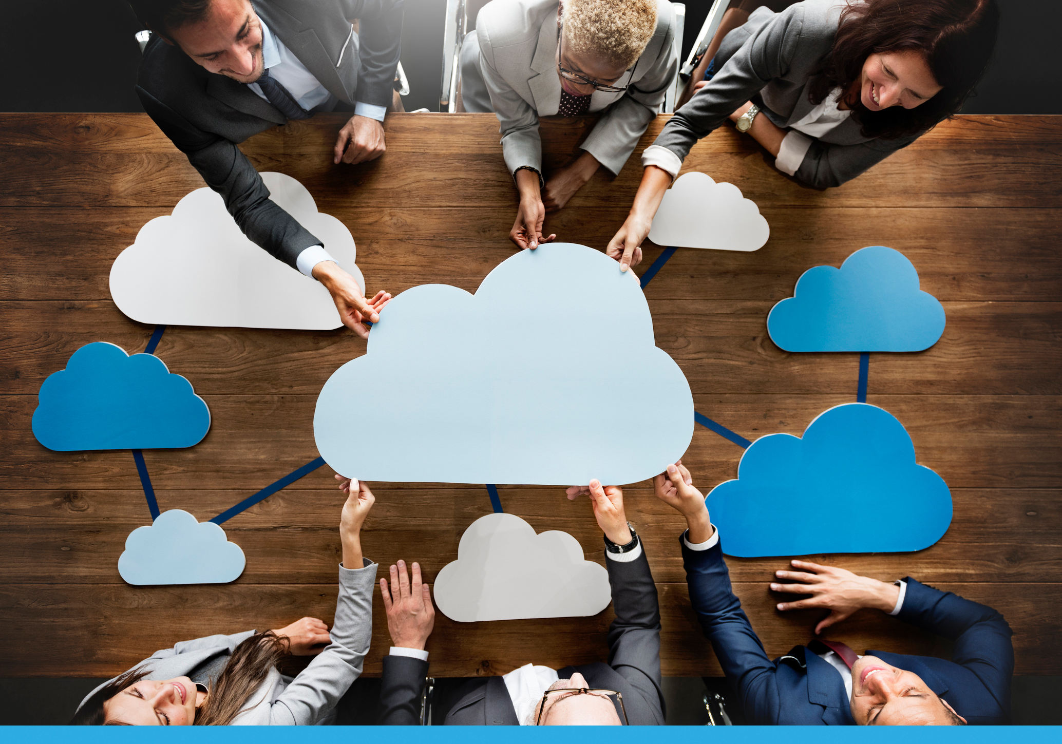 A Blog photo featuring a table with multiple cartoon clouds and people seated at the table reaching for the cloud in the middle.