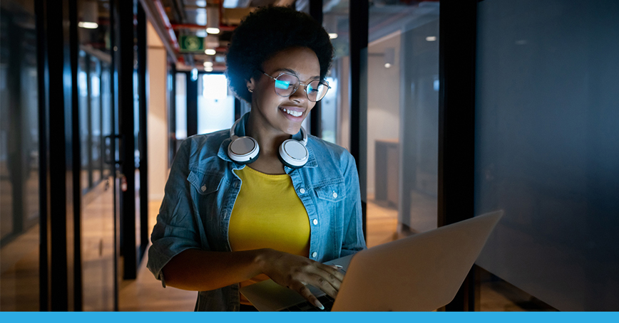 A Blog photo featuring a woman walking in an office hallway while working on her laptop.